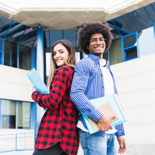 写真 大学キャンパスの前で背中合わせに立っている多民族の男性と女性の学生