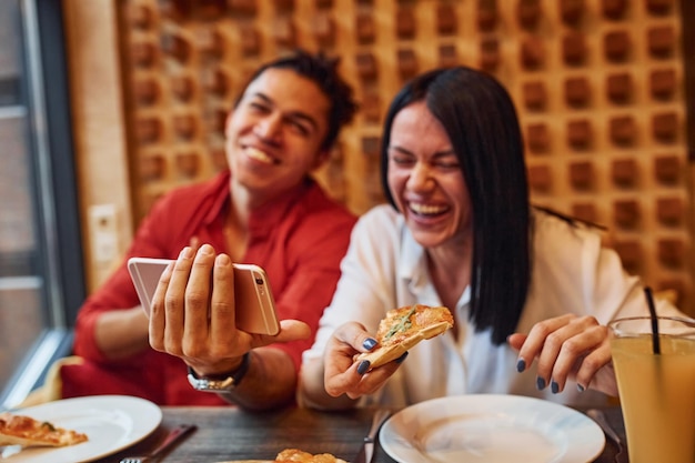 Multi ethnic young couple sitting indoors together and eating pizza.