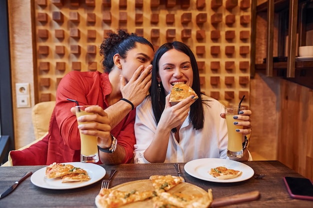 Мультиэтническая молодая пара вместе сидит в помещении и ест пиццу.