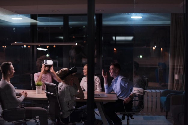 Multi-etnisch Business-team dat virtual reality-headset gebruikt in een nachtelijke kantoorvergadering Ontwikkelaars ontmoeten een virtual reality-simulator rond tafel in een creatief kantoor.