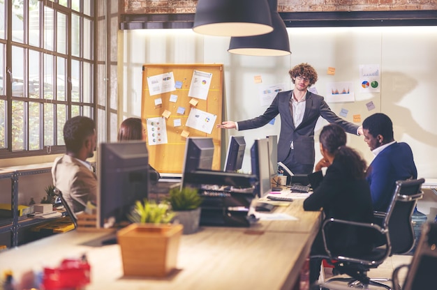 Multi-etnisch business team verschillende kantoormedewerkers praten en glimlachen terwijl ze een vergadering houden met collega's in een modern kantoor, senior zakenman die een achtergrondpresentatie maakt