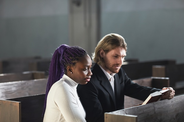 Multi-etnisch jong stel dat samen op de bank zit en samen de Bijbel leest in de kerk