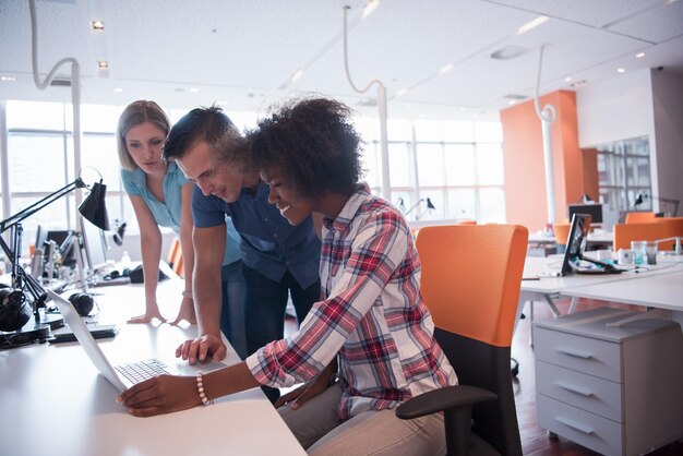 Multi-etnisch opstartend businessteam bij het ontmoeten in modern, helder kantoorinterieur brainstormen, werken op laptop en tabletcomputer