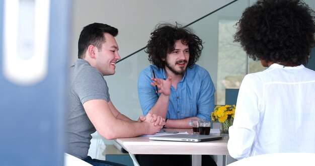 Multi-etnisch opstartend businessteam bij het ontmoeten in modern, helder kantoorinterieur brainstormen, werken op laptop en tabletcomputer