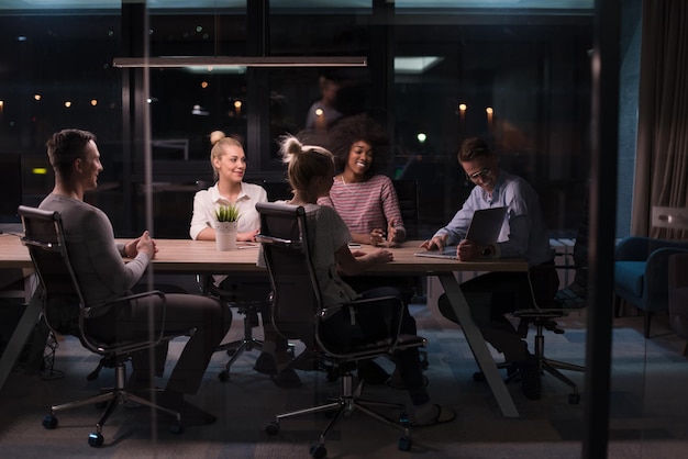 Multi-etnisch startend zakelijk team over ontmoeting in moderne nachtelijke kantoorinterieur brainstormen, werkend op laptop