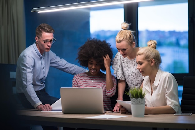 Multi-etnisch startend zakelijk team over ontmoeting in moderne nachtelijke kantoorinterieur brainstormen, werkend op laptop