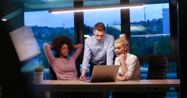 Multi-etnisch startend zakelijk team over ontmoeting in moderne nachtelijke kantoorinterieur brainstormen, werkend op laptop