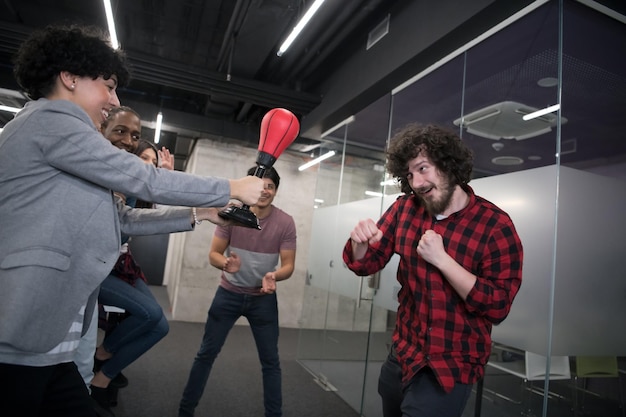 multi-etnisch startend zakelijk team van softwareontwikkelaars die plezier hebben tijdens het boksen op kantoor, opgewonden diverse werknemers die lachen genieten van grappige activiteit tijdens werkpauze, creatieve vriendelijke werknemers spelen