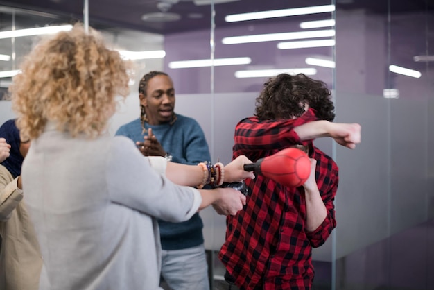 multi-etnisch startend zakelijk team van softwareontwikkelaars die plezier hebben tijdens het boksen op kantoor, opgewonden diverse werknemers die lachen genieten van grappige activiteit tijdens werkpauze, creatieve vriendelijke werknemers spelen