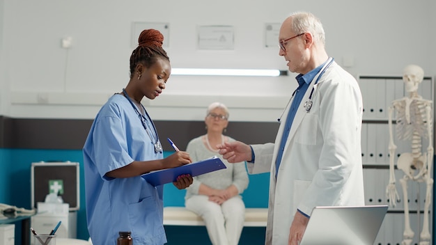 Multi-etnisch team van arts en verpleegkundige die diagnoseresultaten bekijken om behandeling en medicijnen te geven aan senior vrouw in medische kast. Expertise in de gezondheidszorg om ziekte te genezen bij controle.