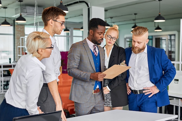 Multi-etnisch vriendelijk team van collega's praten over projecten, zwarte man papier in handen houden