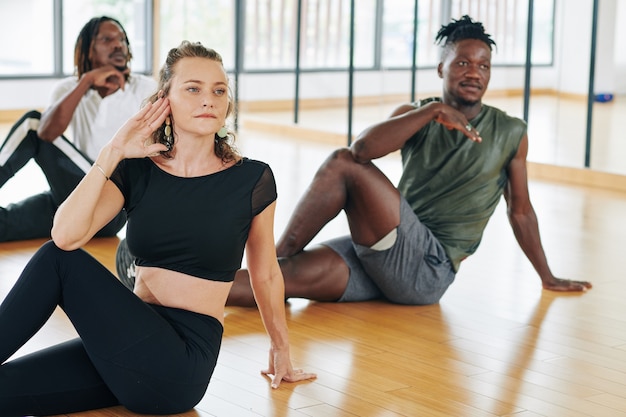 Multi-etnische groep jonge mensen die 's ochtends zittend aan de wervelkolom draaien tijdens het beoefenen van yoga