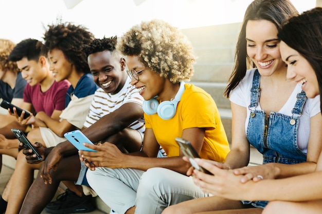 Multi-etnische groep jonge vrienden die mobiele telefoon gebruiken terwijl ze op stedelijke trappen zitten