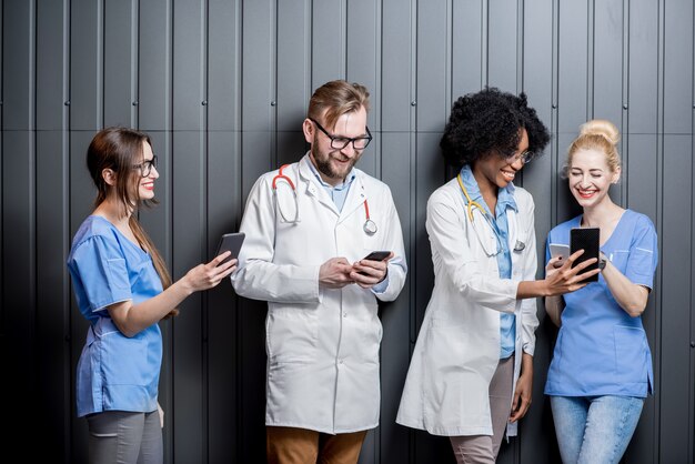 Multi-etnische groep medici die plezier hebben met telefoons op de grijze muurachtergrond