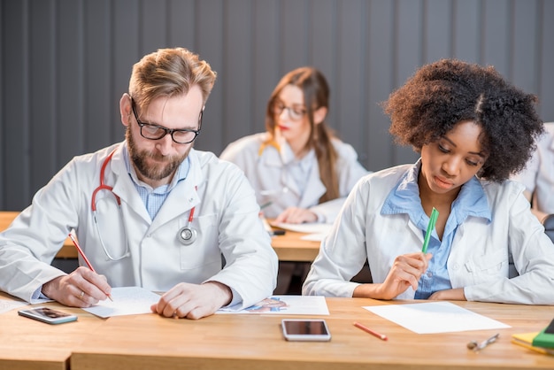 Multi-etnische groep medische studenten in uniform schrijfexamen in het moderne klaslokaal