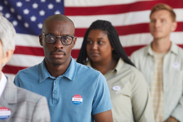 Multi-etnische groep mensen staan in rij bij stembureau op verkiezingsdag, focus op kale afro-amerikaanse man met ik stemde sticker op shirt, kopie ruimte