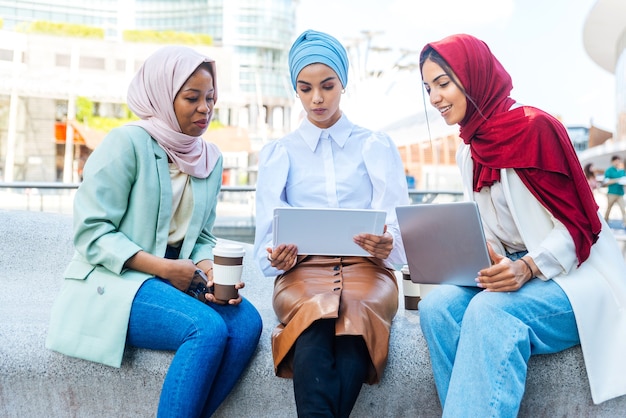 Multi-etnische groep moslimmeisjes die vrijetijdskleding en traditionele hijab-binding dragen en buiten plezier hebben - 3 arabische jonge meisjes