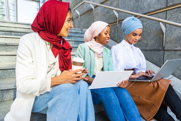 Multi-etnische groep moslimmeisjes die vrijetijdskleding en traditionele hijab-binding dragen en buiten plezier hebben - 3 arabische jonge meisjes