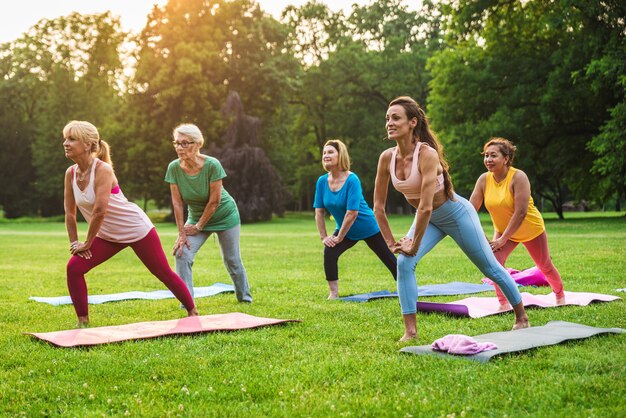 Multi-etnische groep oudere vrouwen die in het park trainen met fitnessinstructeur - Actieve ouderen die sporten in de natuur