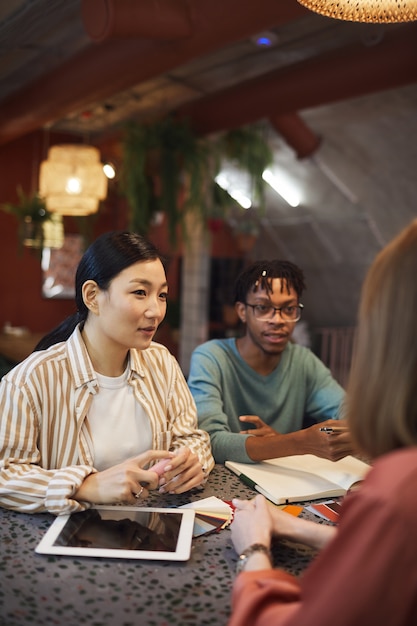 Multi-etnische groep van drie mensen uit het bedrijfsleven werken aan een project zittend aan tafel in café tegen rode muur