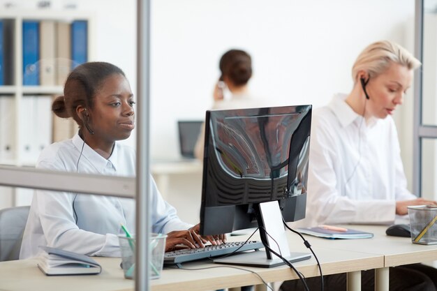 Multi-etnische groep van vrouwelijke call center exploitanten met behulp van computers op de werkplek, focus op jonge afro-amerikaanse vrouw met hoofdtelefoon op voorgrond