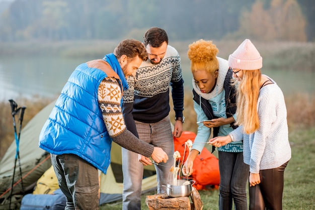 Multi-etnische groep vrienden gekleed in truien die 's avonds fondue eten tijdens de openluchtrecreatie op de camping