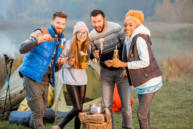 Multi-etnische groep vrienden gekleed in truien die 's avonds fondue eten tijdens de openluchtrecreatie op de camping