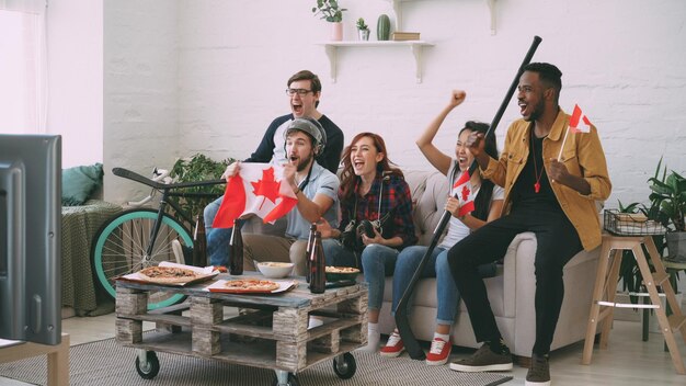 Multi-etnische groep vrienden sportfans met Canadese nationale vlaggen kijken naar hockeykampioenschap