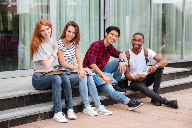 Multi-etnische groep vrolijke jonge studenten die buiten op trappen zitten