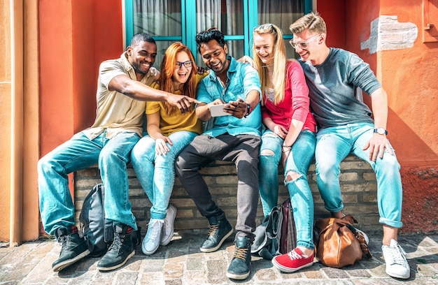 Multi-etnische jongeren die smartphone gebruiken in de achtertuin van een schoolgebouw