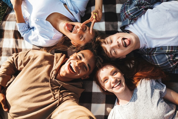 Multi-etnische jongeren jongens en meisjes lachen, en liggend op deken in cirkel buiten