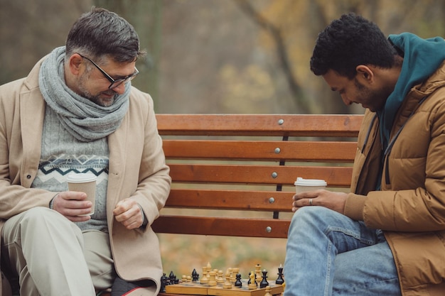 Multi-etnische mannen schaken in herfstpark op een bankje