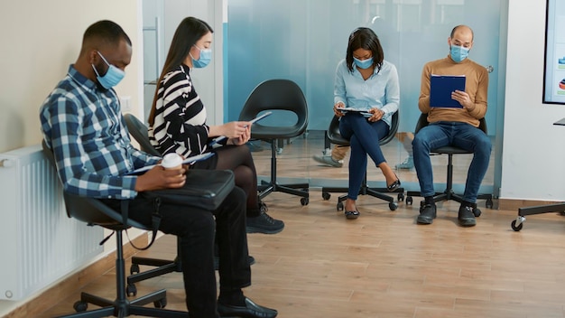 Multi-etnische sollicitanten wachten in de lobby om deel te nemen aan een sollicitatiegesprek tijdens de pandemie van het coronavirus. Nerveuze mensen zitten en voelen zich gestrest over werk en selectie van personeel.