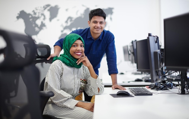 Multi-etnische startup business team Arabische vrouw die een hijab draagt tijdens een ontmoeting in een modern open kantoorinterieur brainstormen, werken op laptop en desktopcomputer