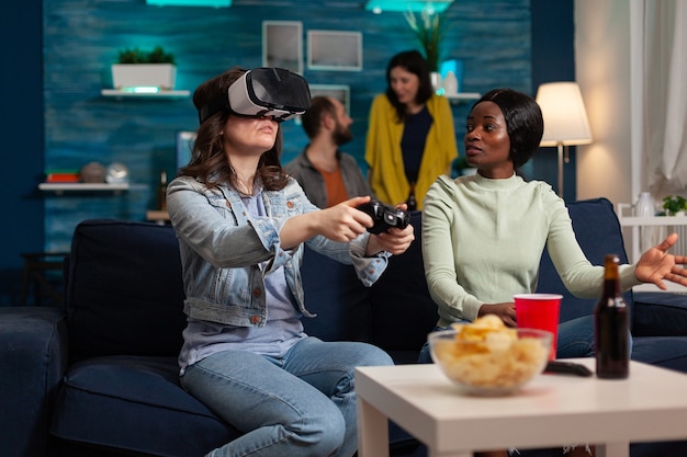 Multi-etnische vrienden die vrouw ondersteunen tijdens videogamecompetitie die met een vr-bril speelt met joystick. gemengd ras groep mensen die samen rondhangen en 's avonds laat plezier hebben in de woonkamer.