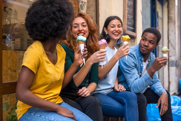 Multi-etnische vrienden in een ijssalon die een ijsje eten, zomerpret kijken elkaar lachend aan