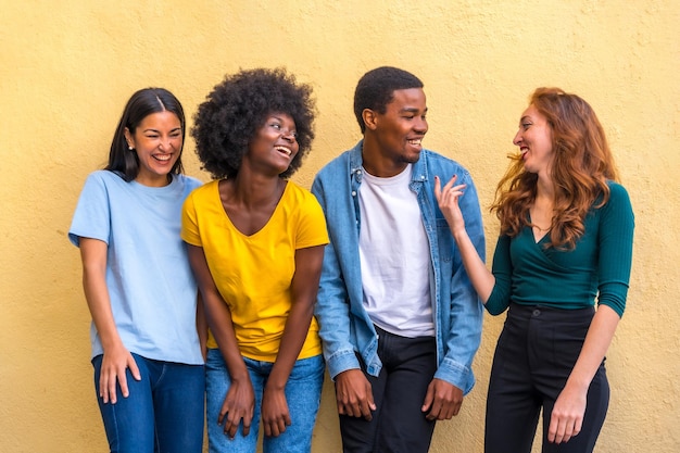 Multi-etnische vrienden tegen gele muur met plezier lachende internationale jeugdgemeenschap