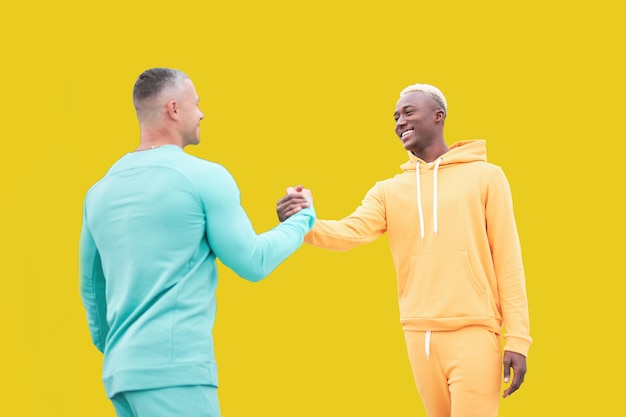 Multi-etnische vrienden. twee mannen verschillende kleur zwart afro-amerikaanse etniciteit en witte blanke etniciteit staande geïsoleerde gele achtergrond. handdruk. interraciale vriendschap