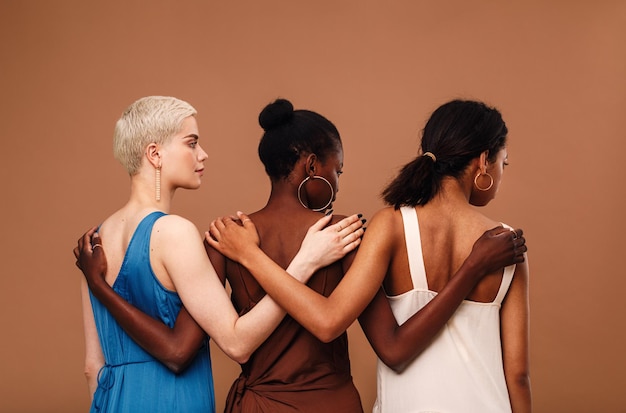 Multi-etnische vrouwen met een arm rond staan tegen een bruine achtergrond