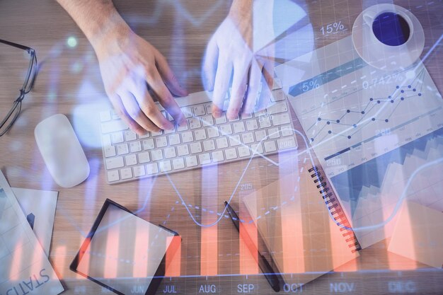 Multi exposure of man's hands typing over computer keyboard and forex graph hologram drawing Top view Financial markets concept