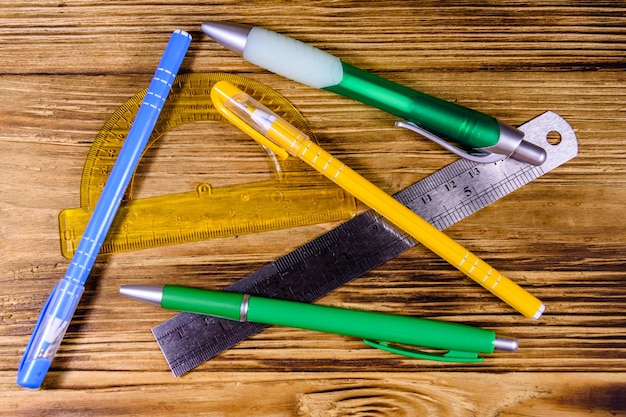 Multi gekleurde balpennen gradenboog en liniaal op rustieke houten tafel bovenaanzicht