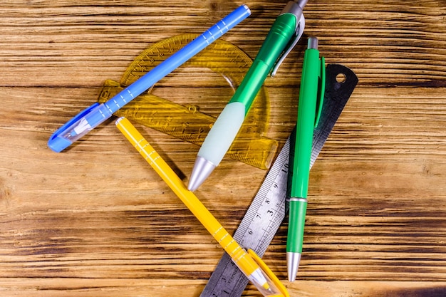 Multi gekleurde balpennen gradenboog en liniaal op rustieke houten tafel bovenaanzicht