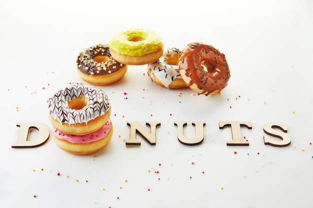 Multi gekleurde donuts met suikerglazuur, hagelslag en de inscriptie donuts op witte achtergrond.