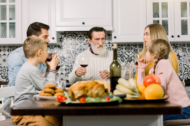 多世代家族がグラスを上げて、感謝祭のディナーテーブルで乾杯します。祖父、親と子が一緒に夕食をとる