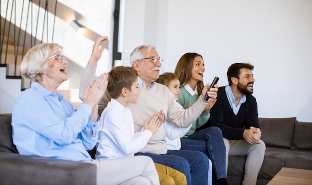 Multi generation family sitting together on the sofa at modern home and watching TV