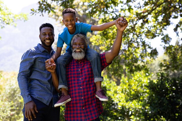 Multi-generation mixed race family enjoying their time at a garden, a mixed race boy is sitting on his grandfather shoulders, looking at the camera and smiling