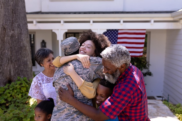 晴れた日に庭で時間を楽しむ多世代の混血家族が、軍服を着たアフリカ系アメリカ人男性を迎え、家族を抱きしめながら帰宅する