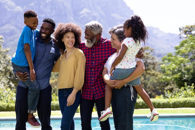 Multi-generation mixed race family enjoying their time at a garden with a pool, standing by the pool, embracing, looking at each other and smiling