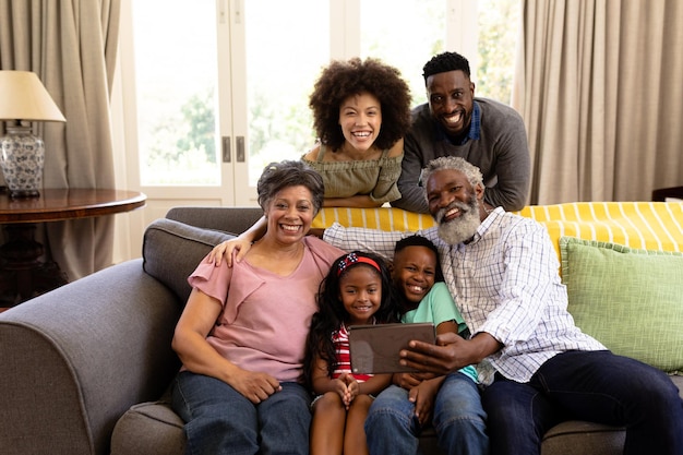 Семья смешанной расы, состоящая из нескольких поколений, вместе проводит время дома, сидит на диване, делает селфи, обнимается и улыбается