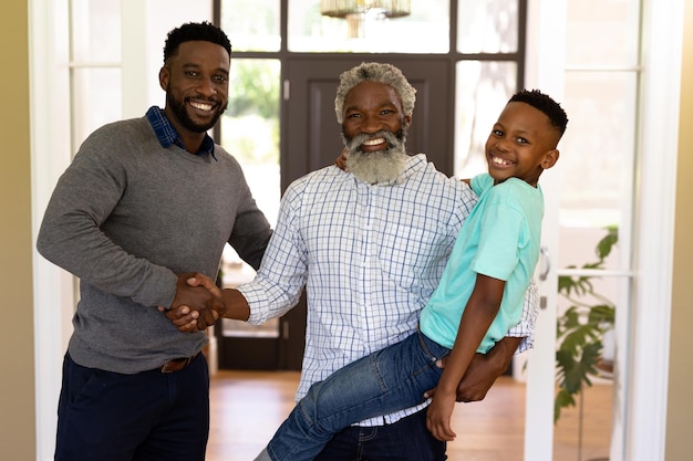 Multi-generation mixed race family enjoying their time at home together, standing in a hallway, shaking hands, looking at the camera, embracing and smiling